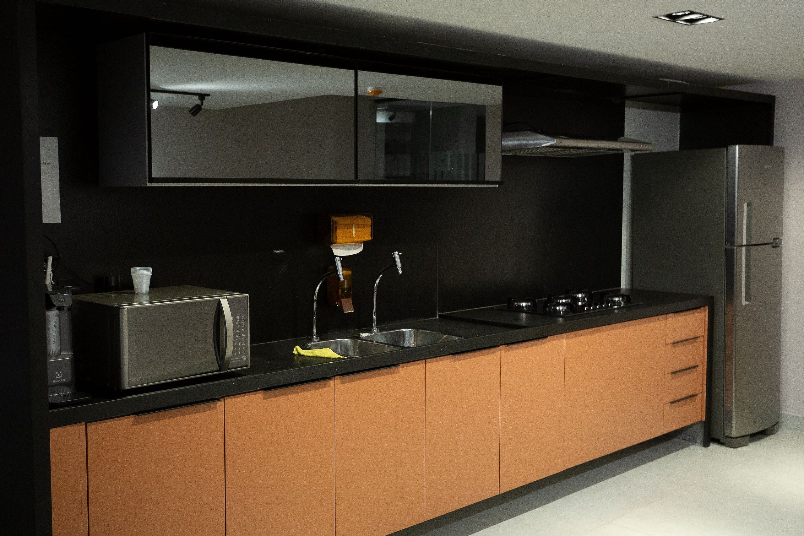 Cozinha moderna com micro-ondas, pia e geladeira de aço inoxidável.