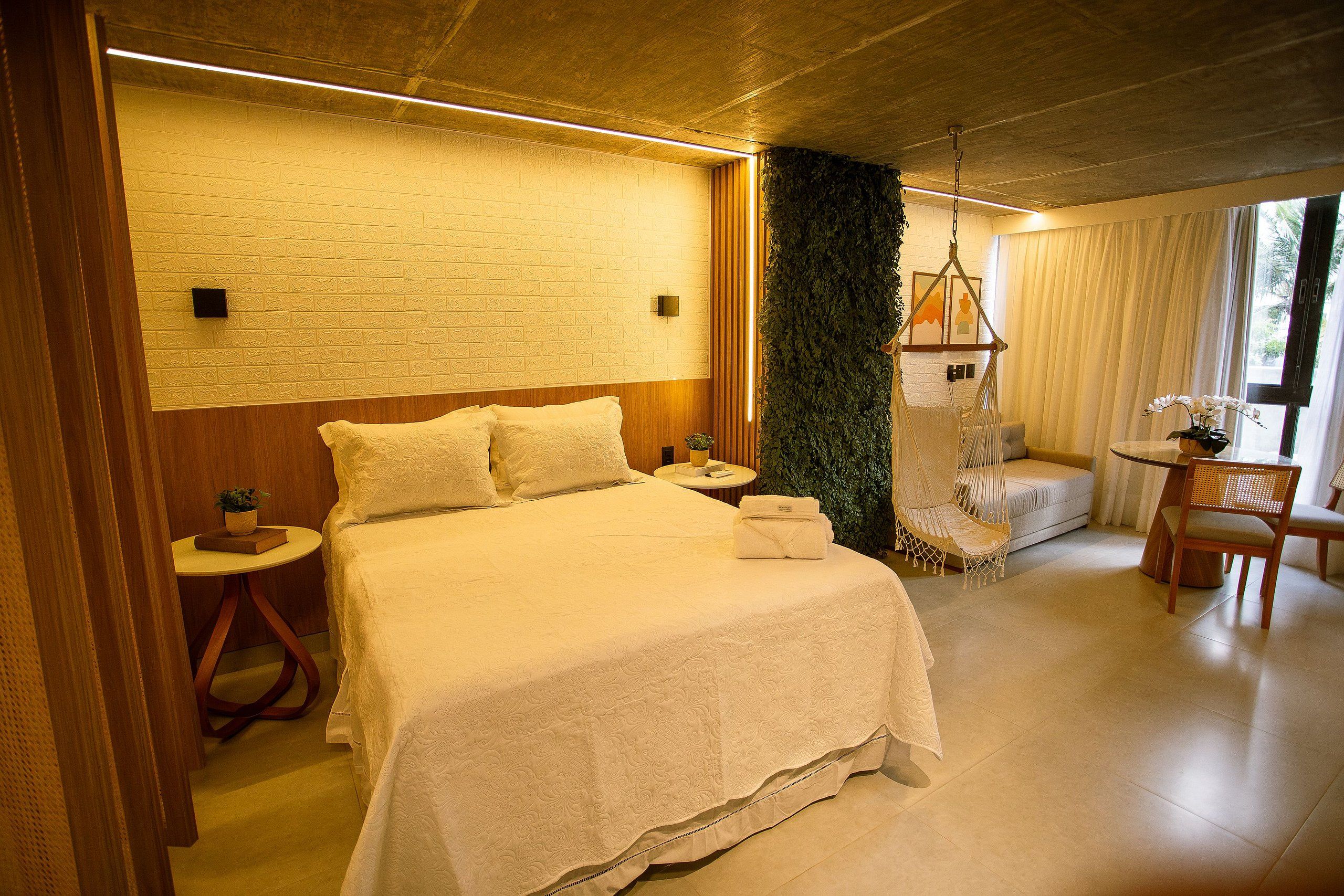 Quarto de hotel com uma cama grande, mesas de cabeceira, uma cadeira suspensa e vista para o exterior.
