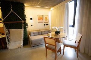 Una sala de estar moderna con una silla colgante, un sofá, una mesa de comedor con sillas y vistas al exterior a través de una ventana.