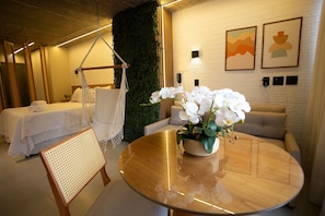 Ein modernes Hotelzimmer mit einem Bett, einem Hängesessel, einem runden Tisch mit Blumenvase und einem Sofa.