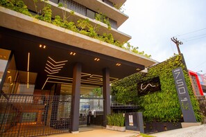 Un edificio moderno con entrada de vidrio, un muro verde con plantas e indicación de la dirección.