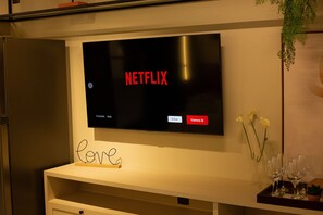 A television displaying the Netflix logo, a white console with a 'love' sign, and a tray with wine glasses and flowers. - Urban #105 - Quadruple in Tambau by Carpediem (João Pessoa)