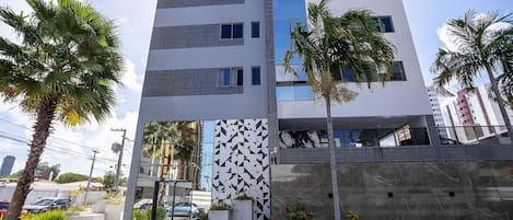 A modern multi-story building with a geometric patterned facade, a glass entrance, and surrounding greenery.