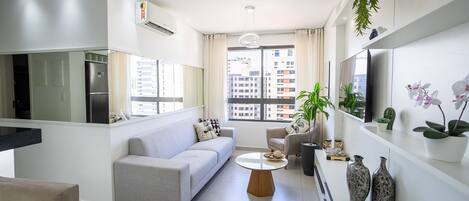Een moderne woonkamer met een bank, salontafel, televisie en decoratieve planten.