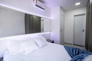 Ein Hotelzimmer mit einem großen Bett, einem Nachttisch, einem Spiegel, einer Klimaanlage und einer Tür.
