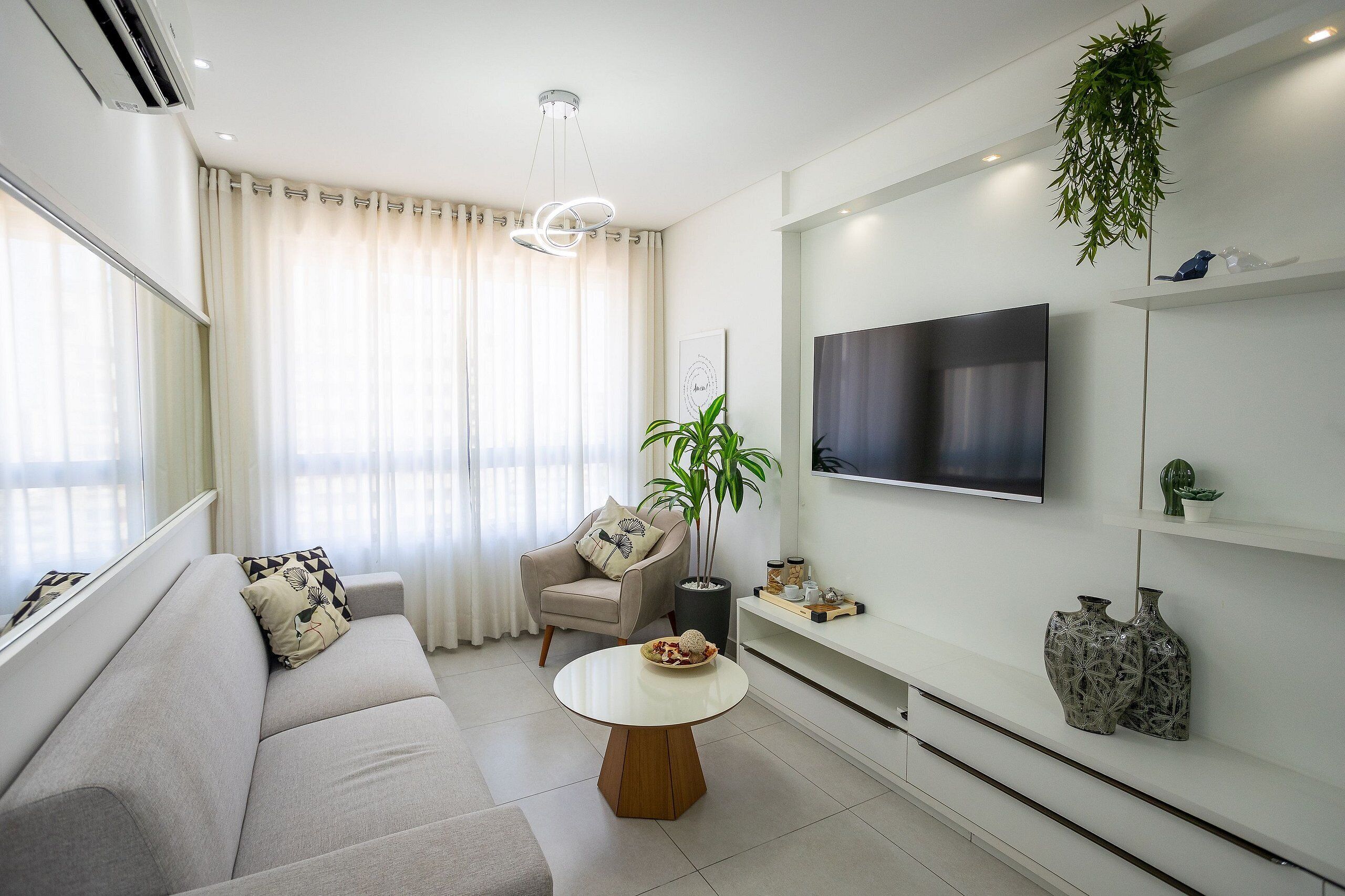 Un salon moderne avec un canapé, une table basse ronde, un téléviseur fixé au mur et une plante en pot.