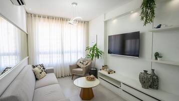 Un salon moderne avec un canapé, une table basse ronde, un téléviseur fixé au mur et une plante en pot.