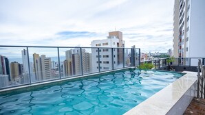 Piscina no terraço com vista para a cidade, cercada por edifícios altos.