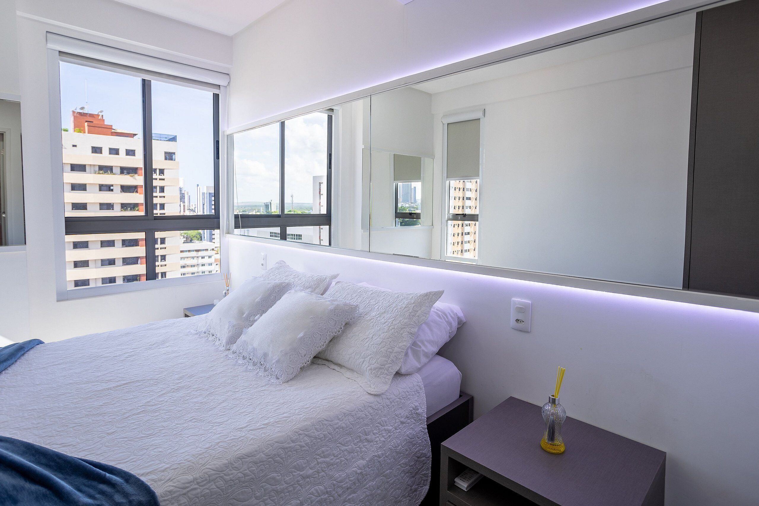 Une chambre avec un grand lit, une table de chevet, un miroir et une fenêtre donnant sur la ville.