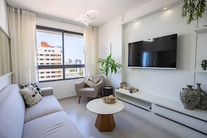 A modern living room with a sofa, armchair, round coffee table, TV, and city view. - Tropical Hub #1002 - Apartment in Manaira by Carpediem (João Pessoa)