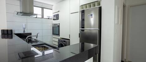 A modern kitchen with a stainless steel refrigerator, microwave, oven, and a built-in washing machine.