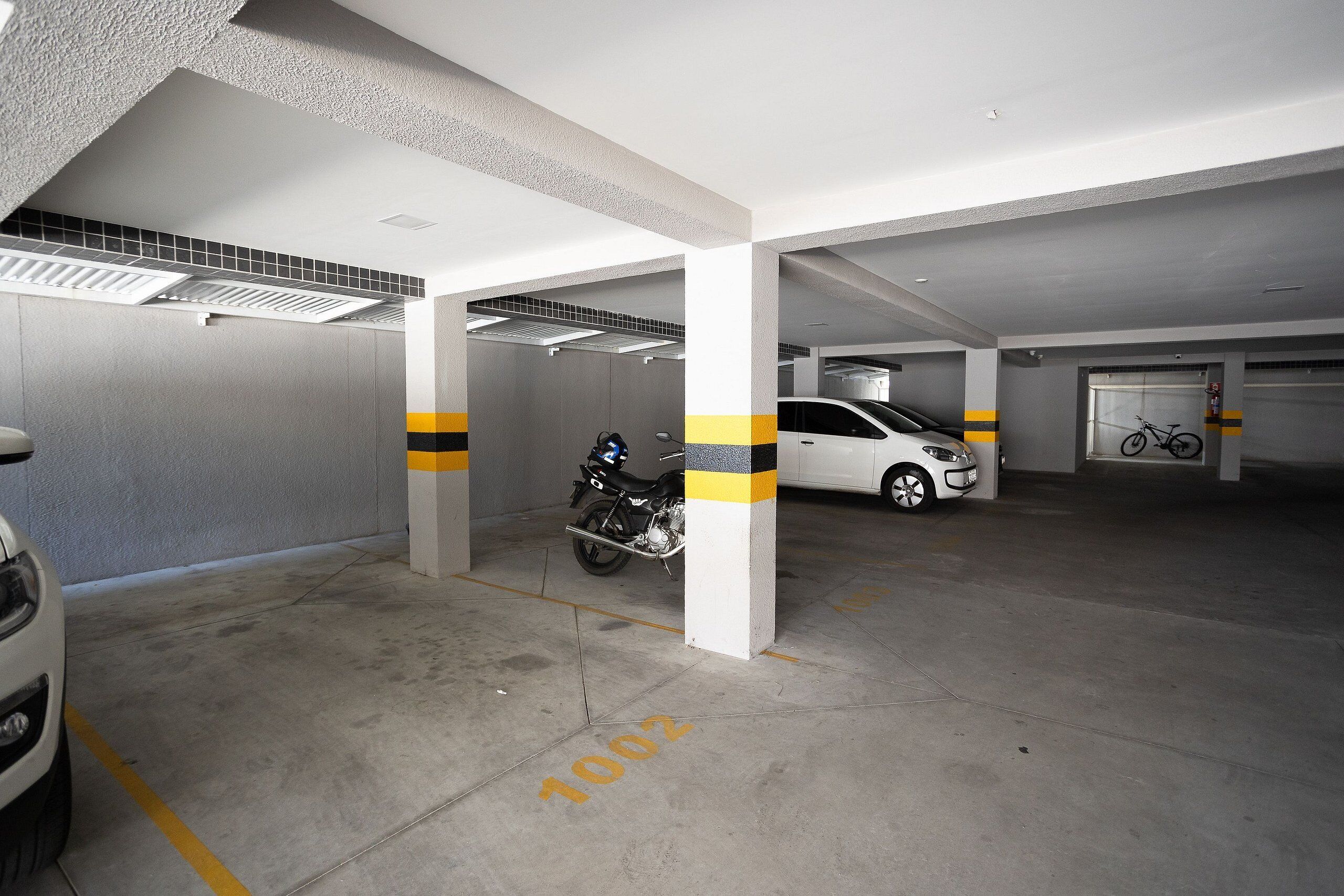 Un parking avec des planchers en béton, des piliers blancs et des bandes jaunes.