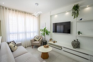 A modern living room with a sofa, a round coffee table, a TV mounted on the wall, and a potted plant. - Tropical Hub #1002 - Apartment in Manaira by Carpediem (João Pessoa)