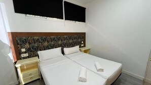 Uma cama de casal com duas mesas de cabeceira, cabeceira com padrão de folha e uma janela com persianas.