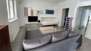 Uma sala de estar moderna com um sofá cinzento, uma televisão de tela plana, um sofá branco e uma mesa de centro de madeira.