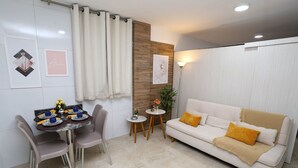 A modern living room with a white sofa, a dining table with chairs, and a small side table with a plant. - Studio Manaira #805 - Flat on the Beach by Carpediem (Cabedelo)
