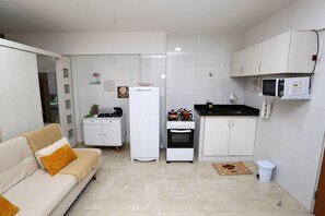 Uma cozinha compacta com armários brancos, uma geladeira, um fogão e um micro-ondas.