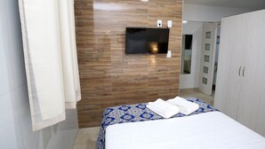 A modern hotel room with a large bed, a flat-screen TV mounted on a wooden wall, and a wardrobe. - Studio Manaira #805 - Flat on the Beach by Carpediem (Cabedelo)
