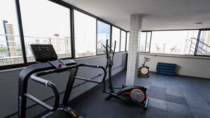 A gym with a treadmill, elliptical, and stationary bike, large windows with a city view, and a tiled floor. - Studio Manaira #805 - Flat on the Beach by Carpediem (Cabedelo)