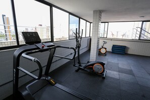 Et fitnesscenter med træningsudstyr, store vinduer og udsigt til bygninger.
