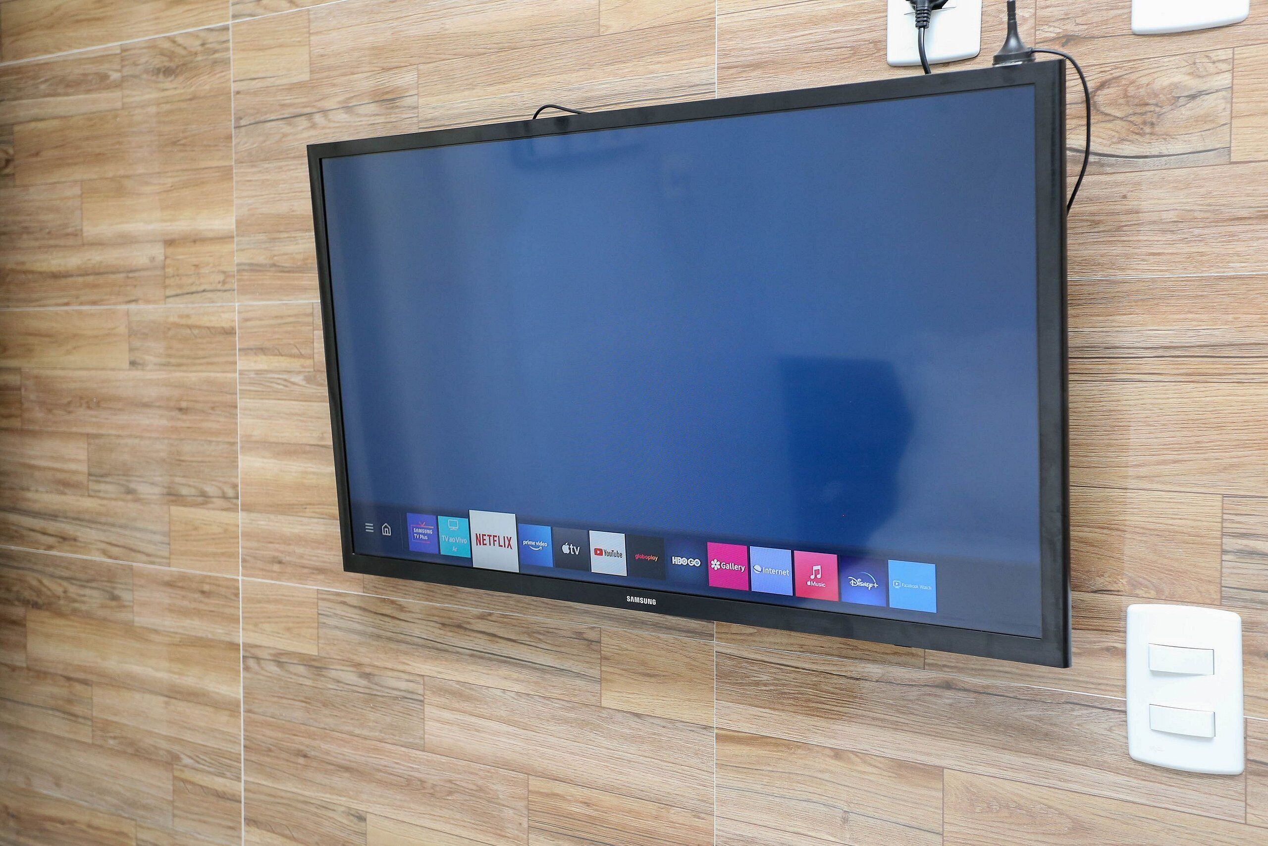 Televisor de pantalla plana montado en una pared de madera, con un enchufe y un interruptor de luz cerca.