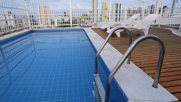 A rooftop pool with blue tiles, white lounge chairs, and a wooden deck. - Studio Manaira #805 - Flat on the Beach by Carpediem (Cabedelo)