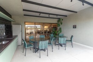 A modern kitchen with a built-in refrigerator, a dining area with round glass tables and wicker chairs, and a large window overlooking the interior. - W Gratitude #1006 - Apartment in Manaira by Carpediem (João Pessoa)