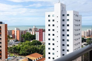 A multi-story building with a white facade, surrounded by other buildings, a clear sky, and a distant view of the sea. - W Gratitude #1006 - Apartment in Manaira by Carpediem (João Pessoa)
