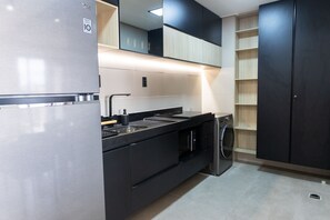 Eine moderne Küche mit Einbauwaschmaschine, einem Edelstahlkühlschrank und schwarzen Schränken.