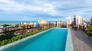 Una piscina sul tetto con vista sulla città, circondata da edifici e vegetazione.