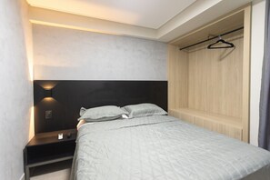 Une chambre à coucher comprenant un lit, des tables de chevet, un porte-manteau et une armoire.