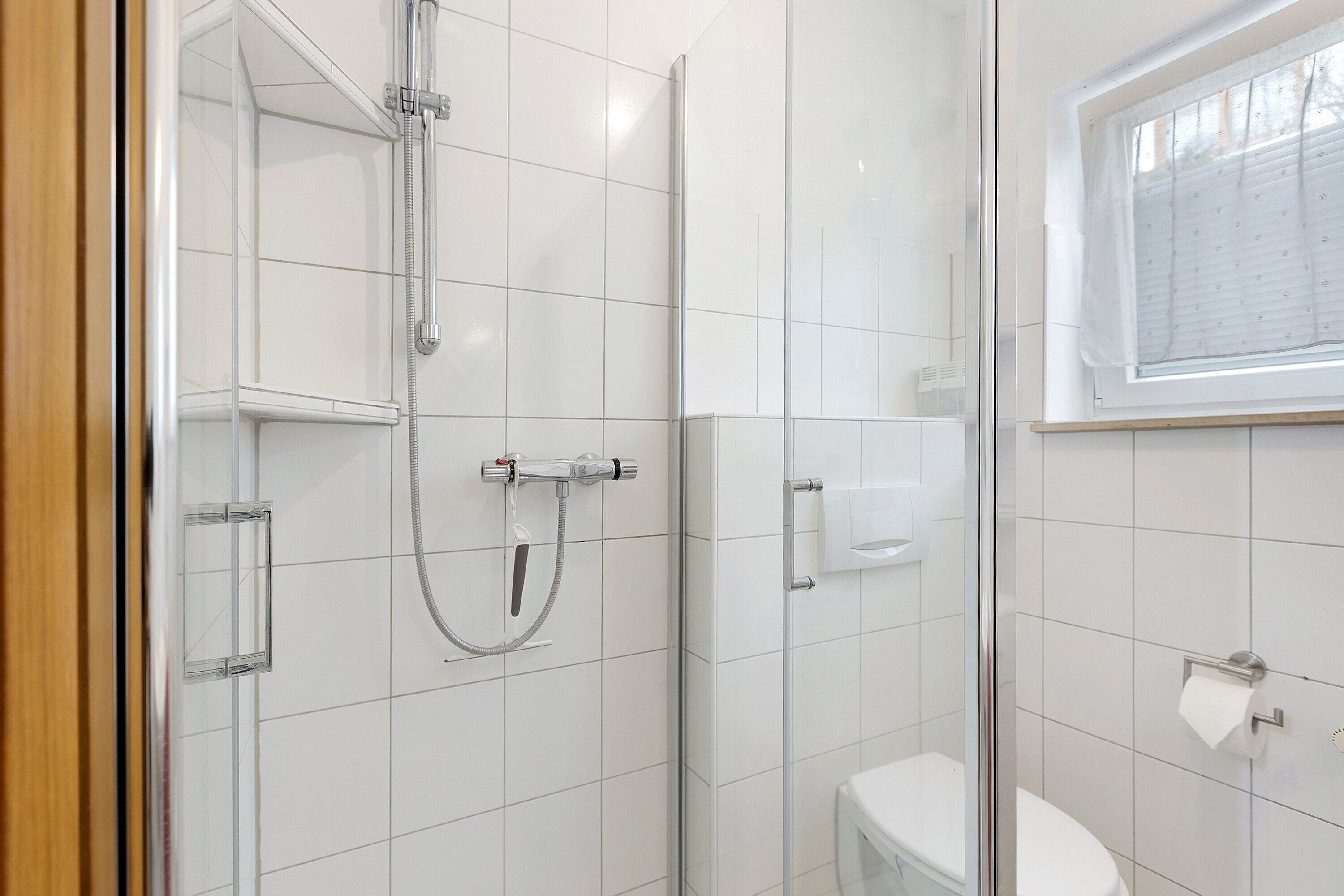 A bathroom with a glass shower enclosure, a toilet, and a window.