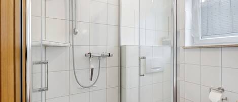 A bathroom with a glass shower enclosure, a toilet, and a window.