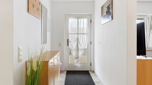 Ein Flur mit einer Holztür, einer schwarzen Matte, einem Holzschrank und einem an der Wand montierten Lichtschalter.