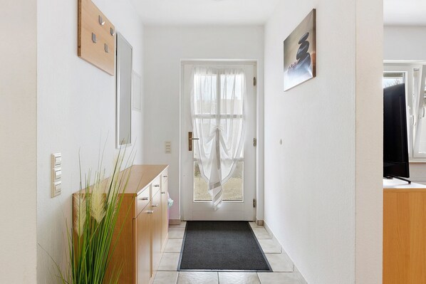 A hallway with a wooden door, a black mat, a wooden cabinet, and a wall-mounted light switch.