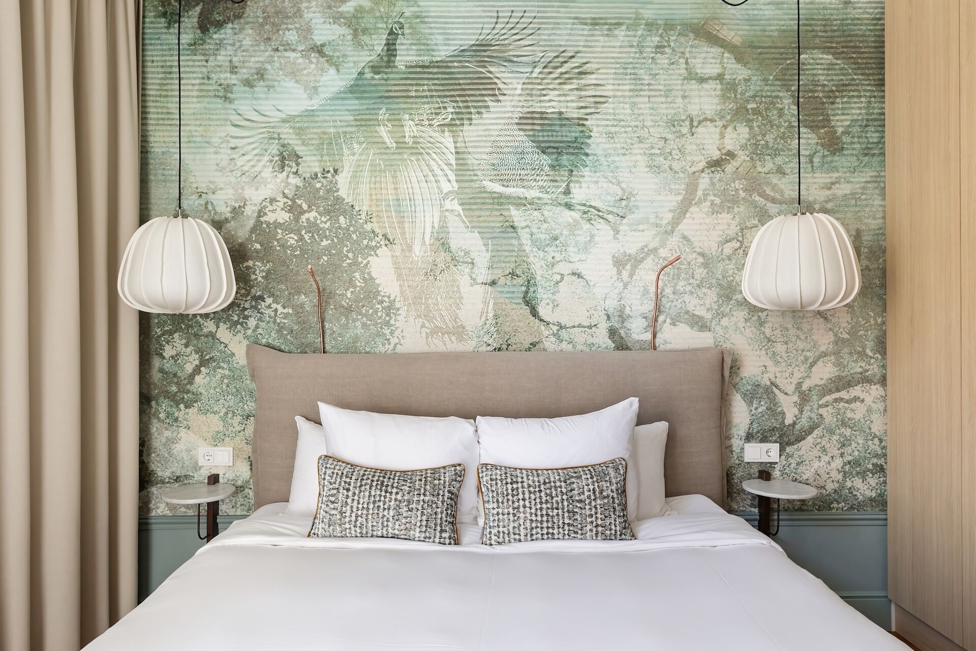 A bedroom with a large bed, two bedside tables, and a headboard with a textured wall mural.