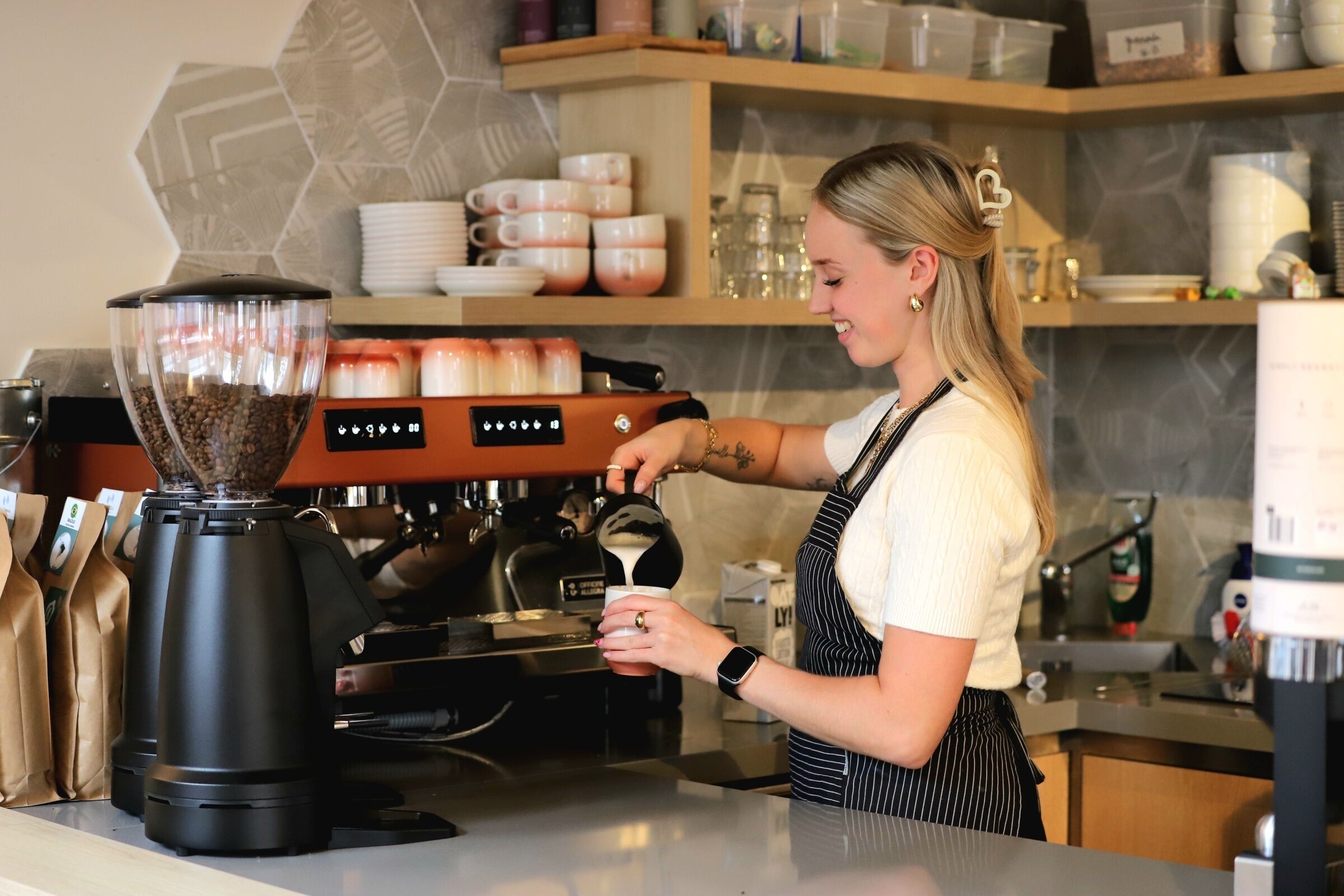 Een koffiezaak met een koffiemolen, een koffieapparaat en een persoon die koffie aan het zetten is.