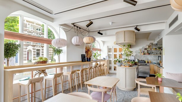 A modern cafe with wooden furniture, a central island, and large windows offering a view of the street. - Hotel Copper (Middelburg)