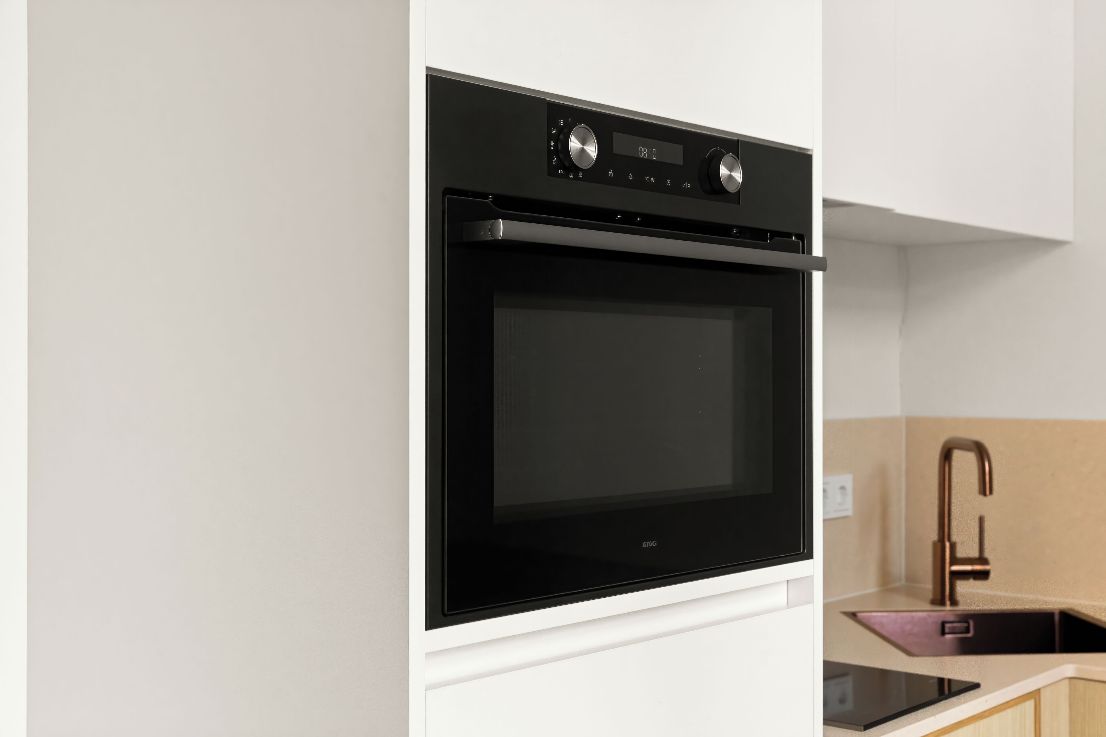 A modern kitchen with a built-in oven, a stainless steel faucet, and a black countertop.