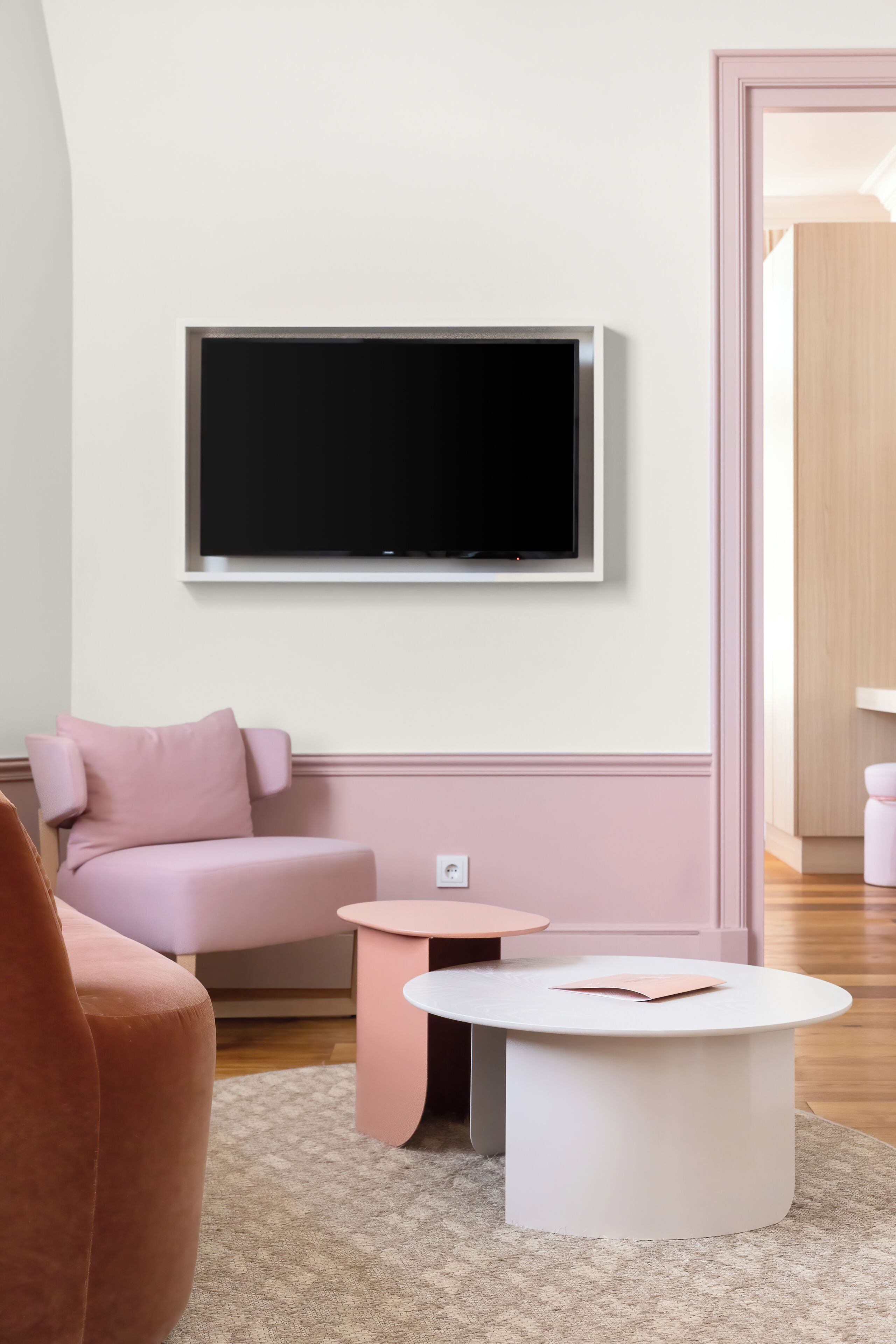 Una sala de estar moderna con un sofá rosa, una mesa de centro blanca y un televisor de pantalla plana montado en la pared.