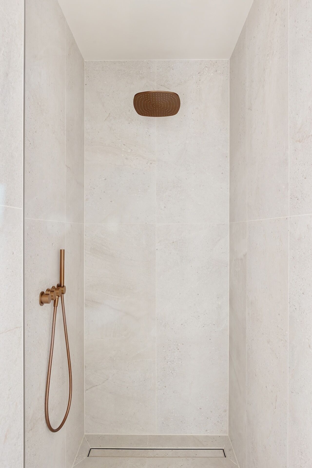 A shower with a handheld showerhead and a wall-mounted control panel.