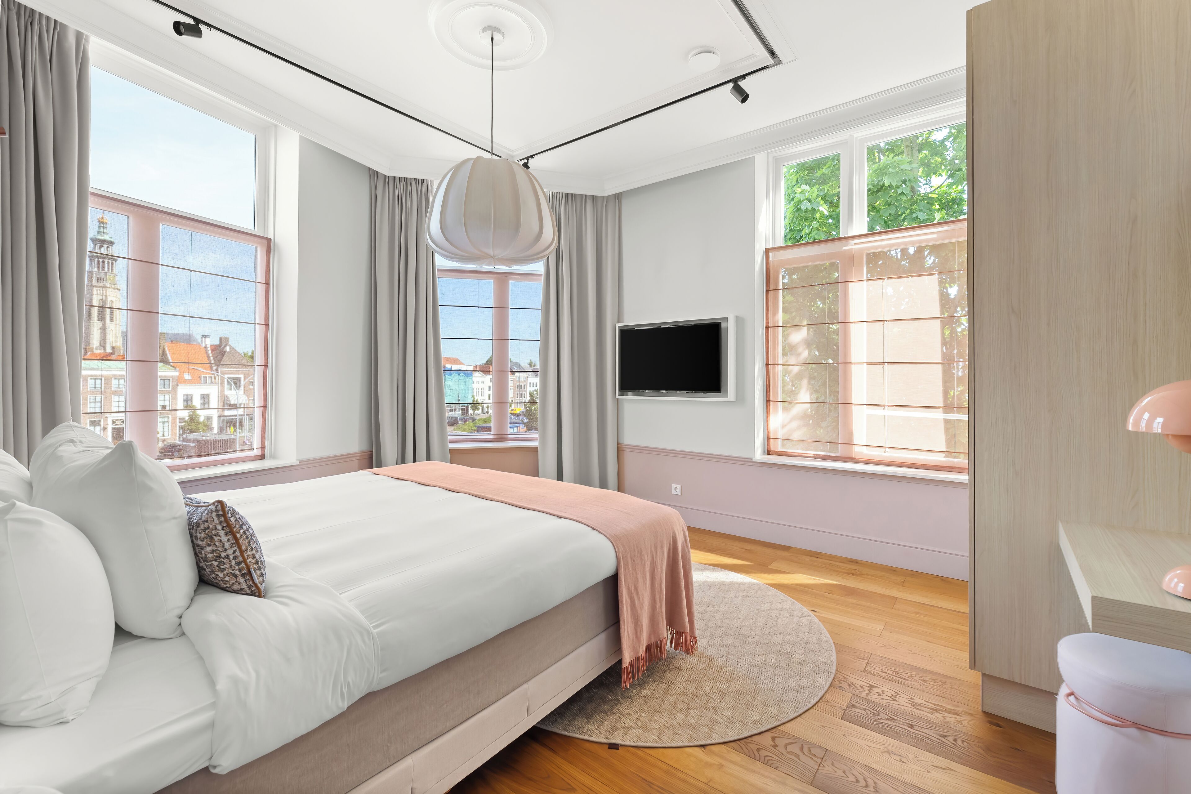 A modern bedroom with a large bed, a TV, and large windows with curtains.