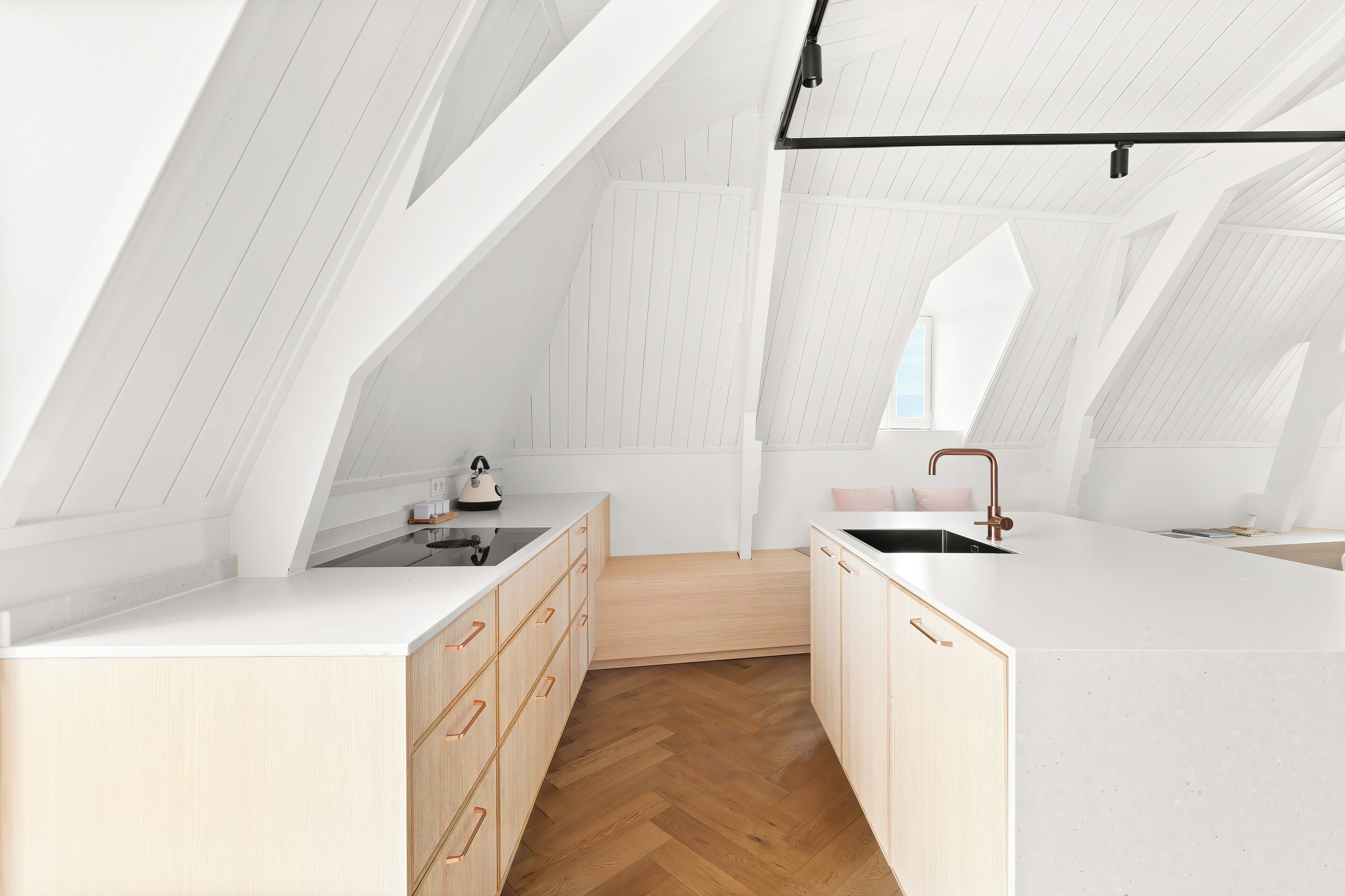 A modern kitchen with white cabinetry, wooden herringbone flooring, and a large island with a sink.
