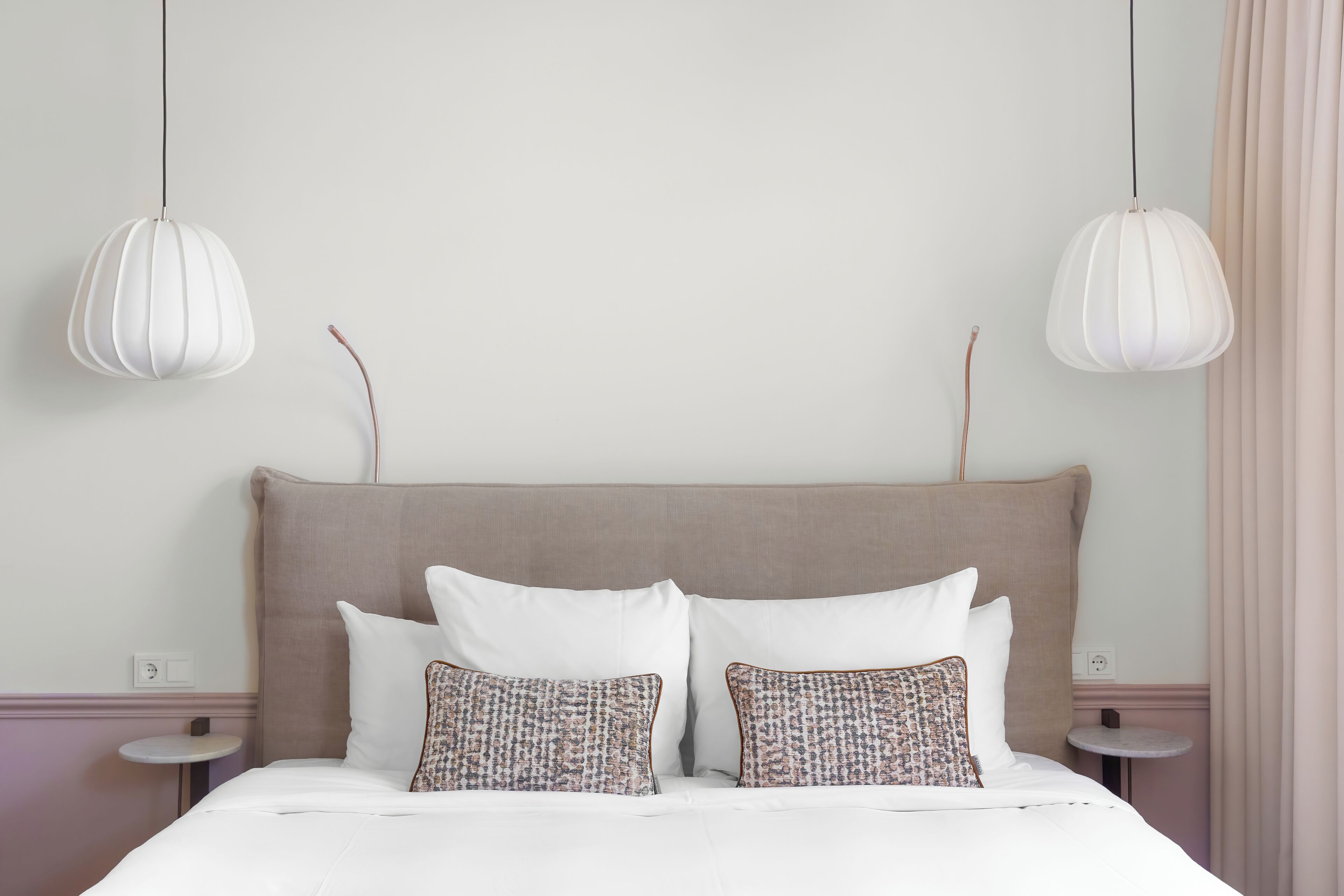 Ein ordentlich bezogenes Bett mit weißen und gemusterten Kissen, eine beige Kopfteil und zwei Nachttische mit Lampen.