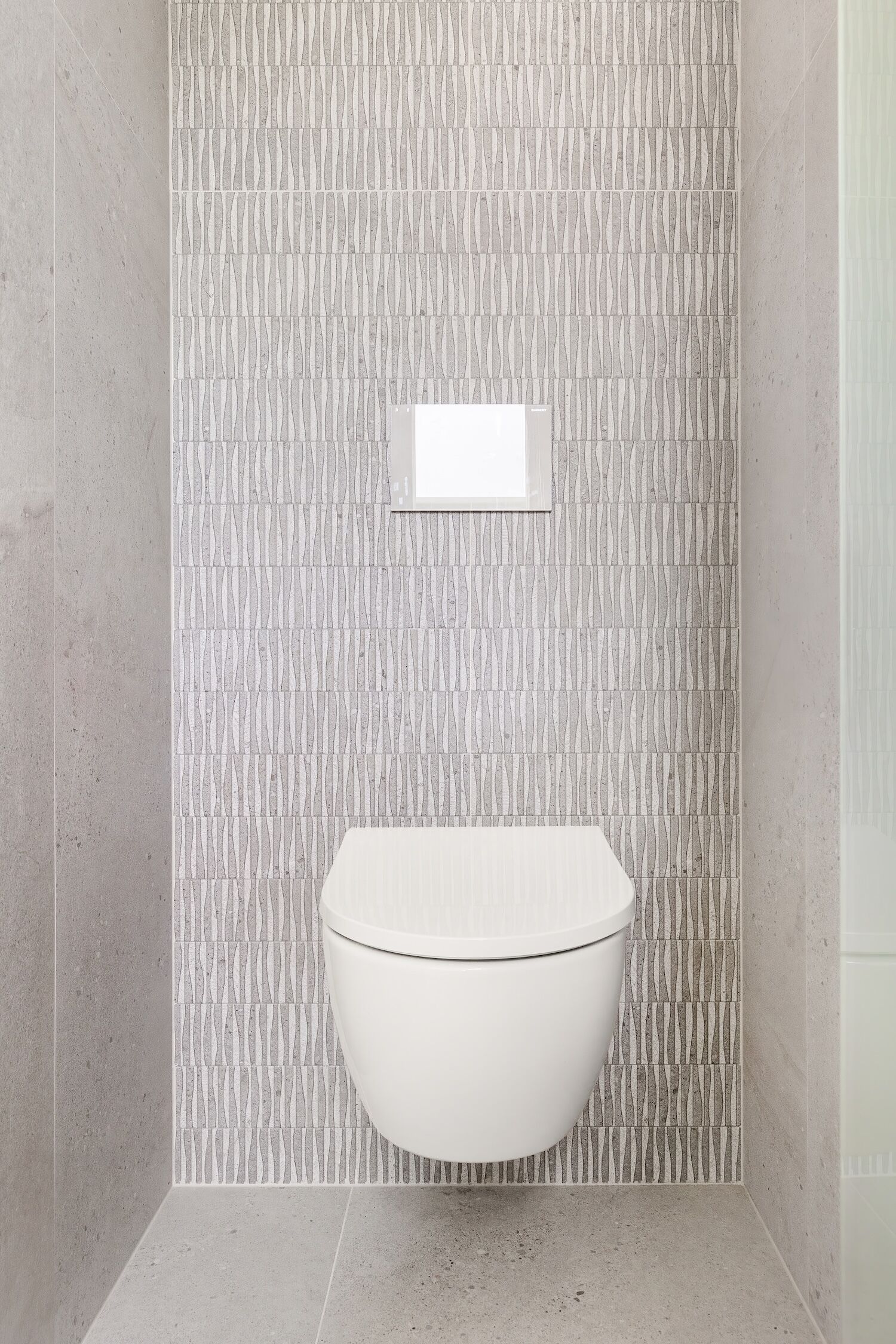 Un baño moderno con inodoro blanco, pared decorada y una ventana pequeña.