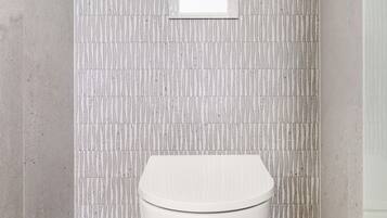 Ein modernes Badezimmer mit Toilette, Wand mit Muster und kleinem Fenster.