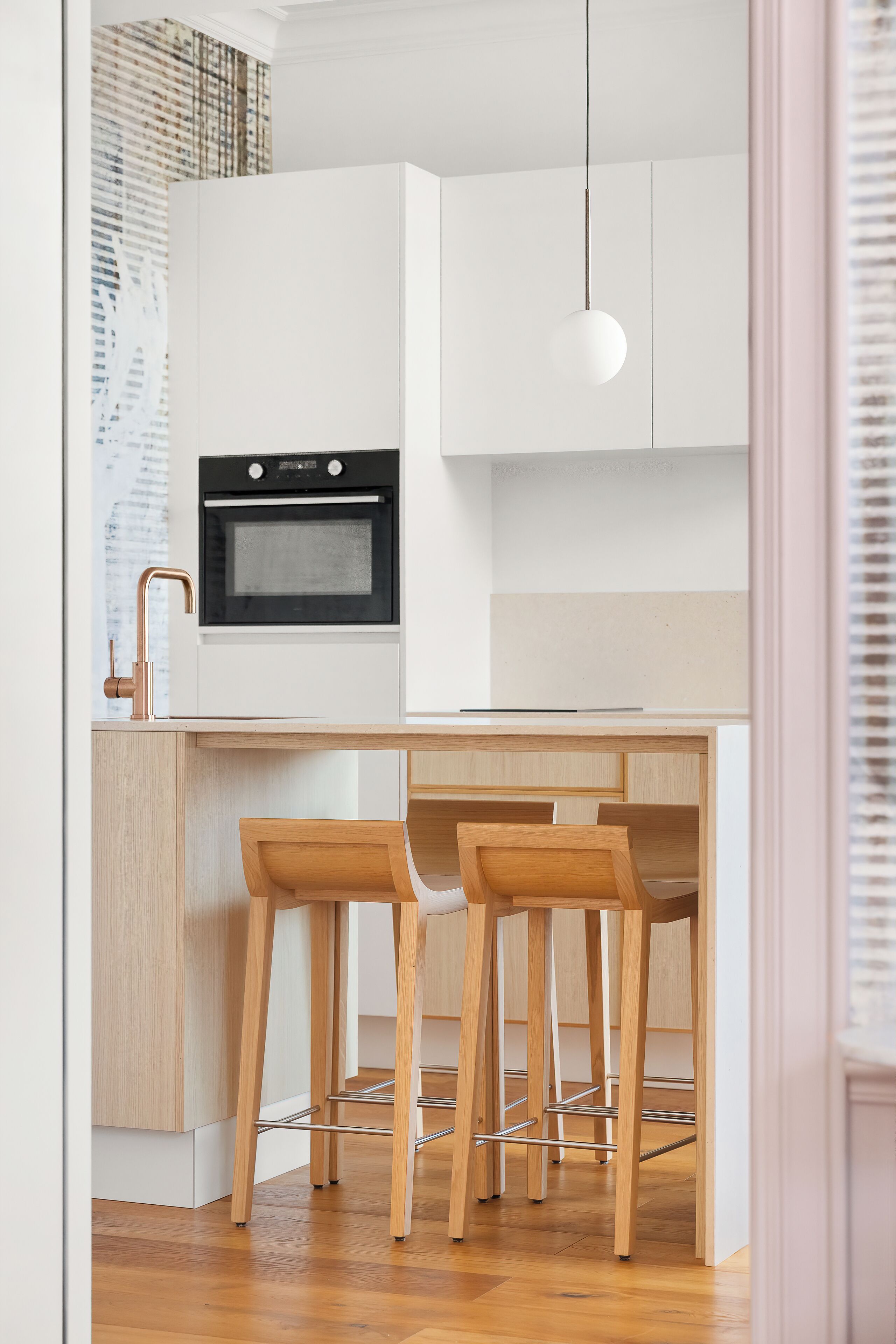 Una cocina moderna con armarios blancos, un horno negro y taburetes de madera.