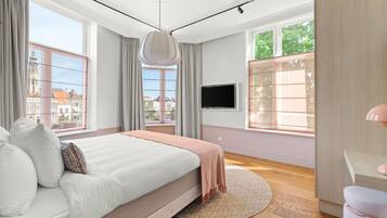 Un dormitorio moderno con una cama grande, televisor y ventanas amplias con cortinas.