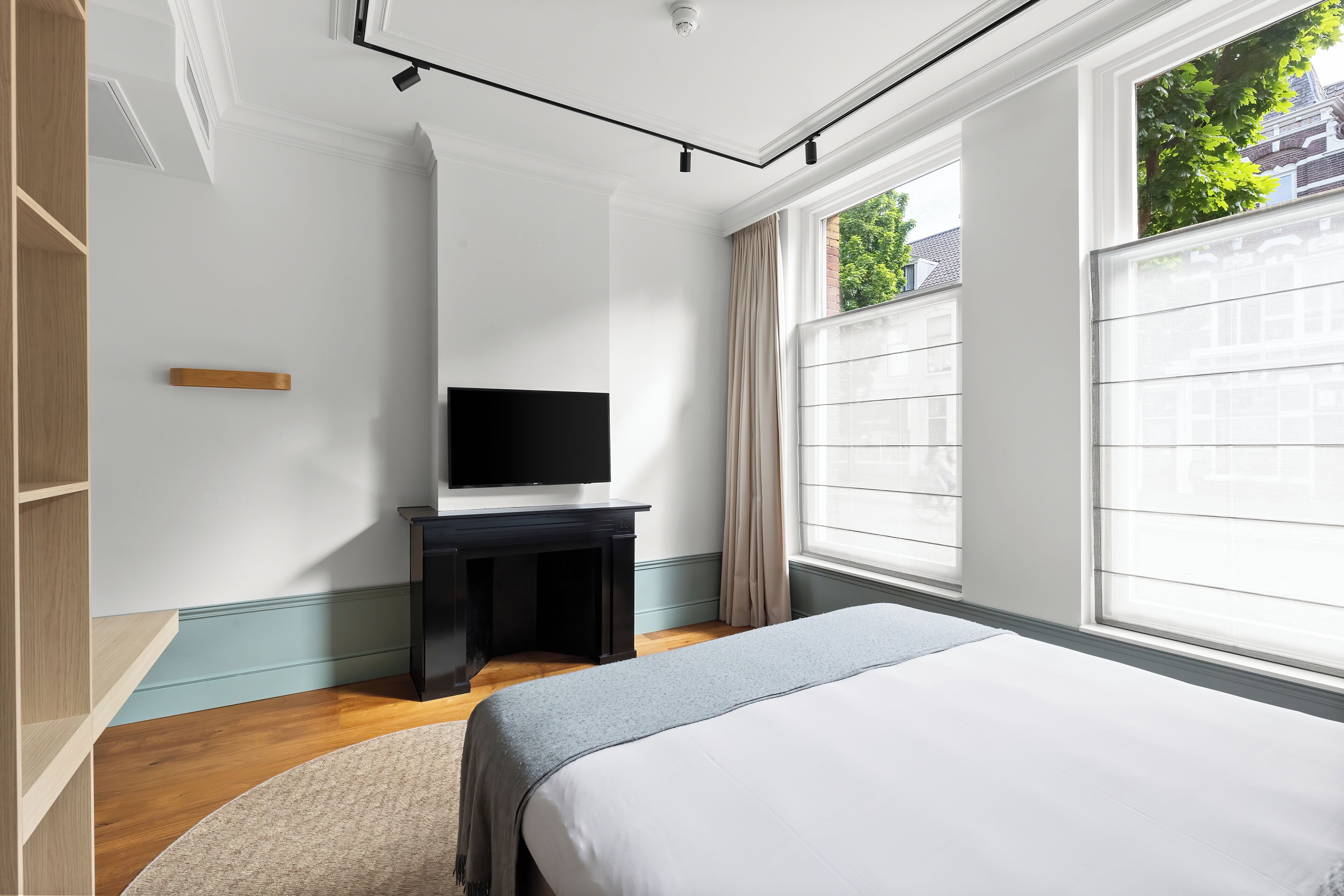 A bedroom with a bed, a TV on a stand, a window with curtains, and a wooden floor.
