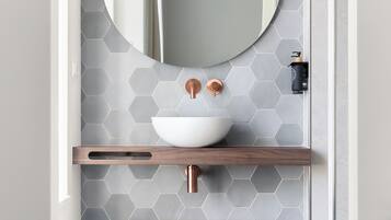 A bathroom with a round mirror, a white sink, and a wooden bench.